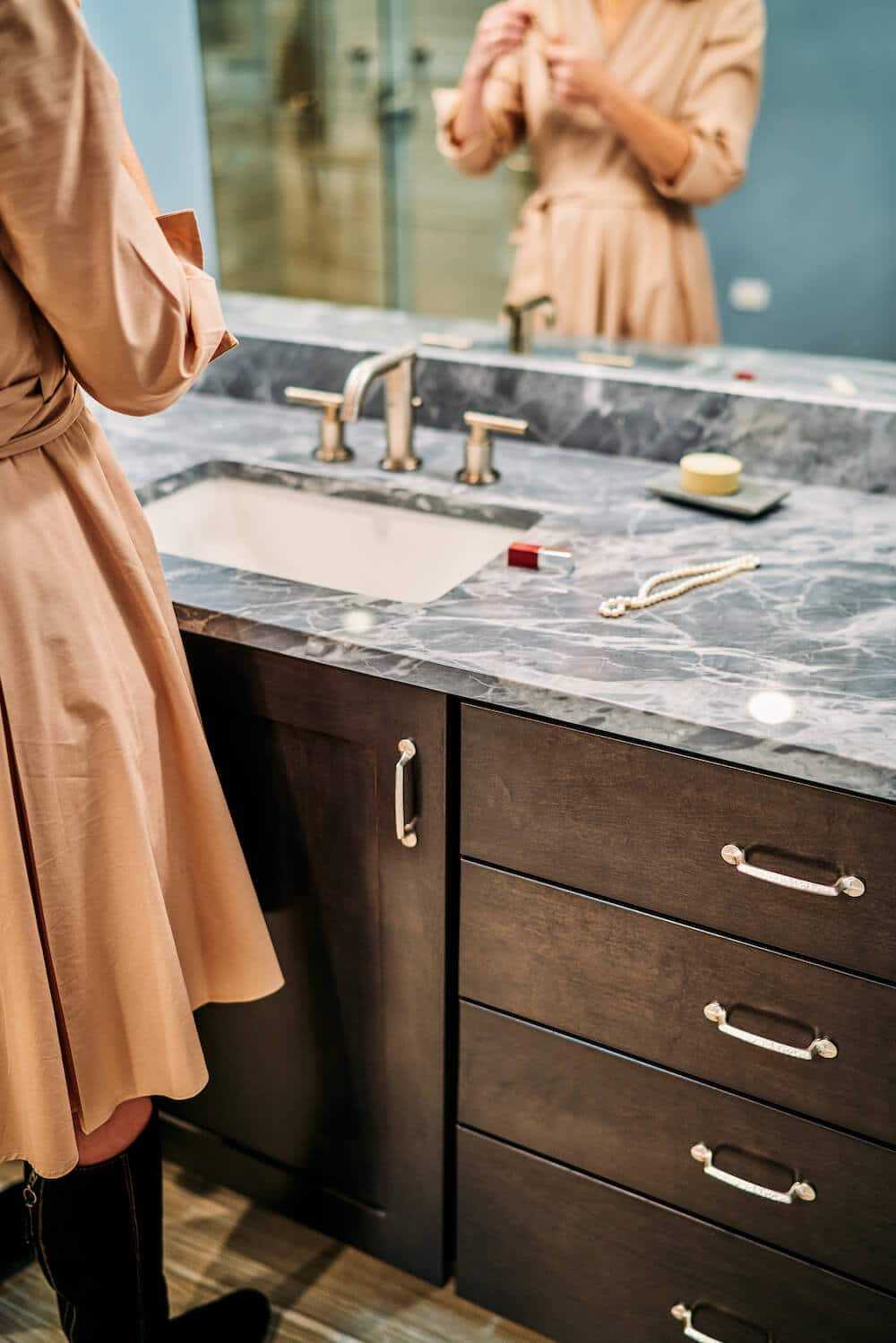 woman applying make-up at bathroom vanity with granite countertop and custom brown bathroom cabinet